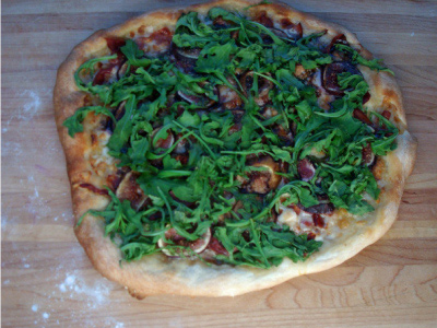 Top down view of finished pizza cut into slices sitting on a wood pizza spatula, sitting on a white wood table.