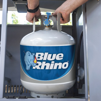 A person inserting a fresh Blue Rhino propane tank into the cabinet of a standup propane grill.