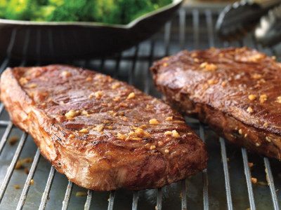 Grilled steaks on a resting grid with a bowl of broccoli.