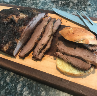 A finished smoked brisket sliced on a wood cutting board on a green and white granite countertop.