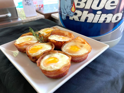 Six bacon and egg cups on a square white plate, sitting on a black table cloth. Fresh Blue Rhino propane tank and standup propane grill in the background.