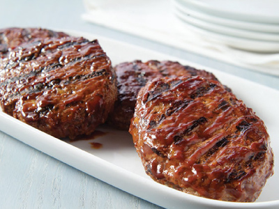 Three grilled steaks on a white plate, sitting on a white tablecloth.