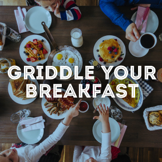 Friends around a wood table with breakfast food on it.