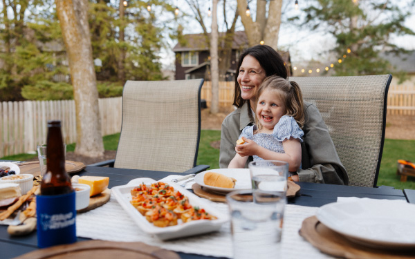 Mother and child sitting at an outdoor patio table with grilled food on it.