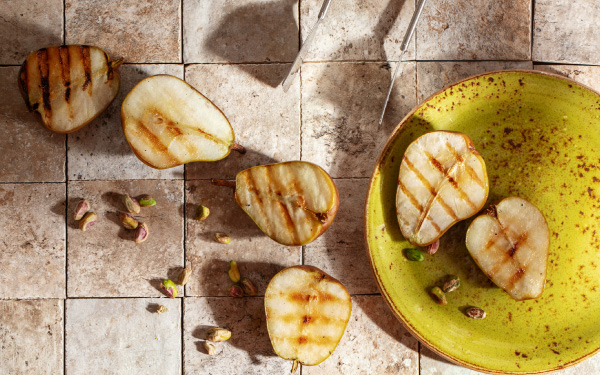 Finished grilled pears on a green plate and on a tile countertop.