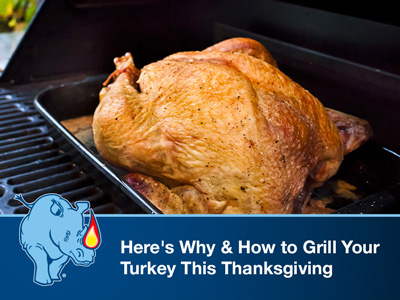 Turkey in a black pan being grilled on a standup propane grill.