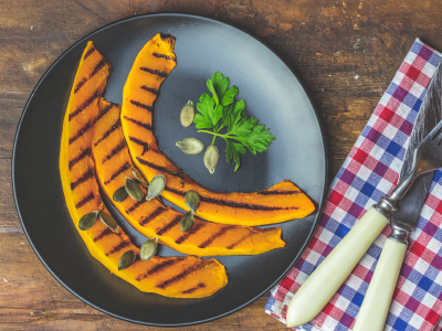 Grilled pumpkin slices on a black plate sitting on a wood table with a red, white, and blue napkin.