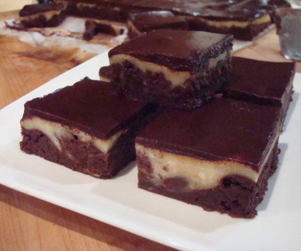 Stack of finished brownies on a white plate, sitting on a wood table.