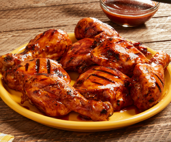 Grilled chicken legs on a yellow plate, sitting on wood table.