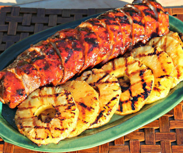 Grilled pork loin and grilled pineapple on a green plate, sitting on a wicker table.