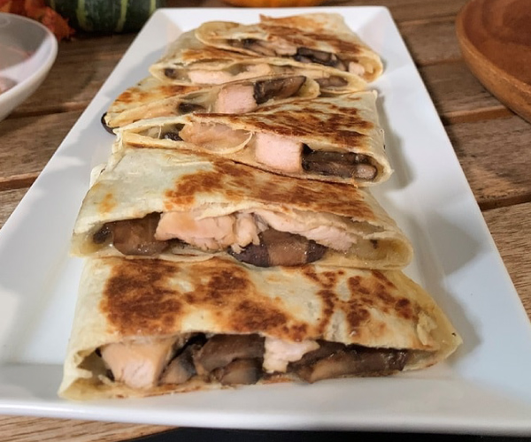 Finished quesadilla cut into slices, stacked onto a white rectangular plate, sitting on a wood table.
