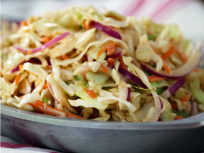 Coleslaw sitting in a gray plate on a red and white tablecloth.