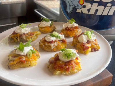 Finished seven Loaded Smashed Potatoes on a white plate, with a fresh Blue Rhino and a standup propane tank in the background.