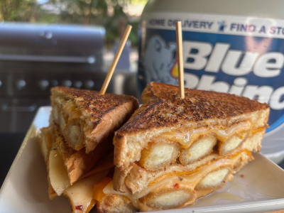 Finished grilled cheese on a white plate, with a fresh Blue Rhino propane tank and standup propane grill in the background.