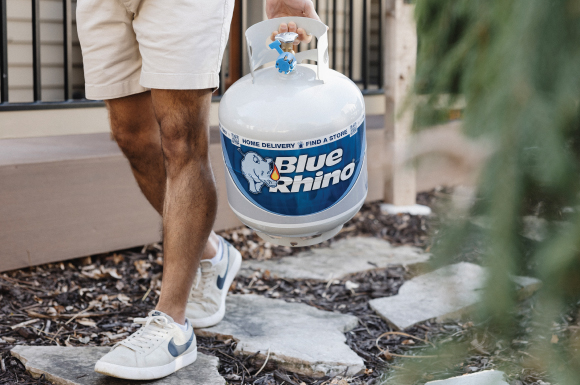 Man carrying fresh Blue Rhino propane tank towards the backyard.