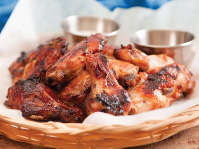 Stack of grilled chicken wings on parchment paper in a bamboo plate holder.