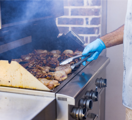 Man grilling chicken on a stainless steel standup propane grill.