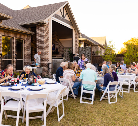 Party guests sitting at tables in the backyard eating food.