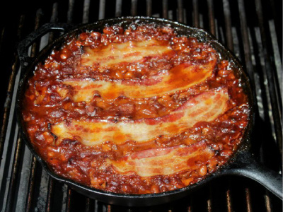 Finished beans in a cast-iron pan on a standup propane grill's cooking grids.