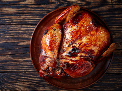 Grilled whole turkey on a red plate, sitting on a wood table.