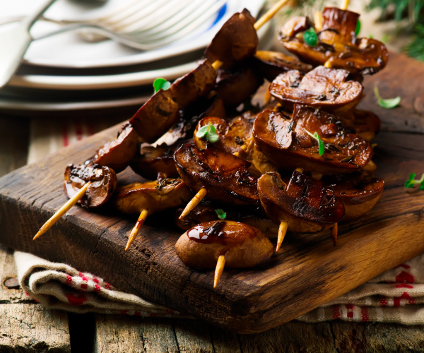 Finished balsamic grilled mushrooms on skewers on a wooden cutting board.