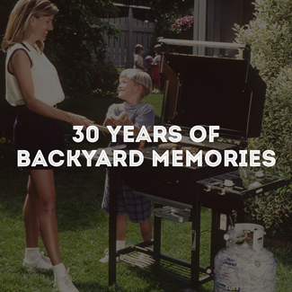 Woman and child standing next to a standup propane grill, grilling food.