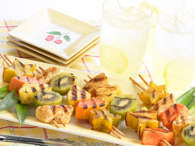 Four skewers on a rectangular white plate, sitting on a yellow table cloth