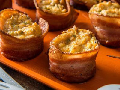 Grilled bacon cups filled with eggs, sitting on a orange sheet.