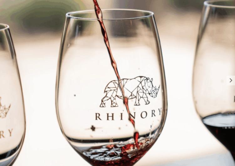 Red wine being poured into one of three glasses with the markings 'Rhinory' on them.