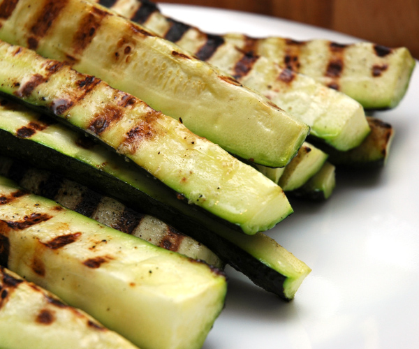 Bunch of grilled zucchini stacked on a white plate.