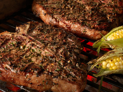 Two steaks being grilled with 2 ears of corn on a grill's cooking grids.