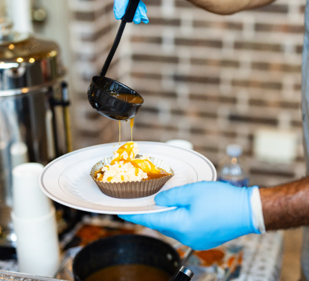 Chef drizzling carmel sauce ontop fresh cupcakes, on a white plate.